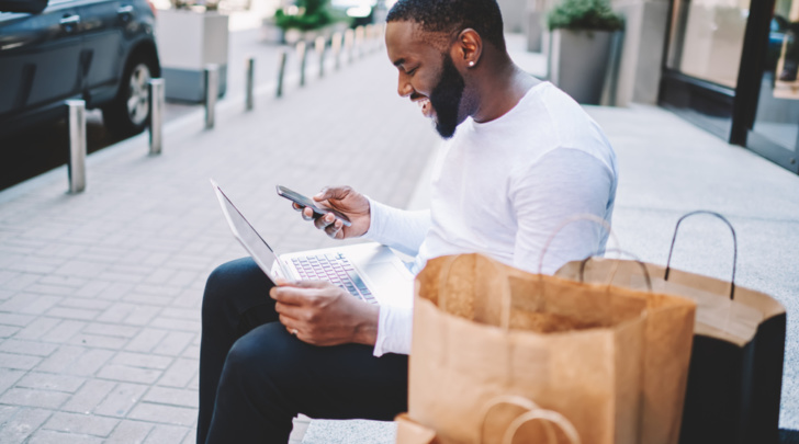 man designing on laptop while completing his purchase journey using his smartphone